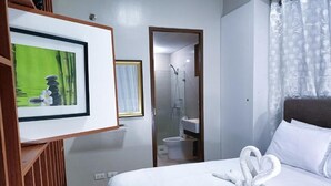 A hotel room with a bed, a framed picture on the wall, a shower area, and a bathroom. - Kim's hub at Two Palmtree Villas (Pasay City)