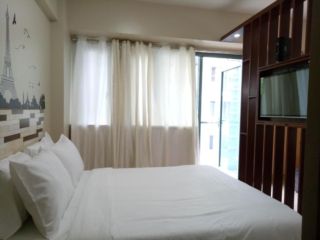 A hotel room with a bed, curtains, a wall with a cityscape mural, and a television on a wooden stand.