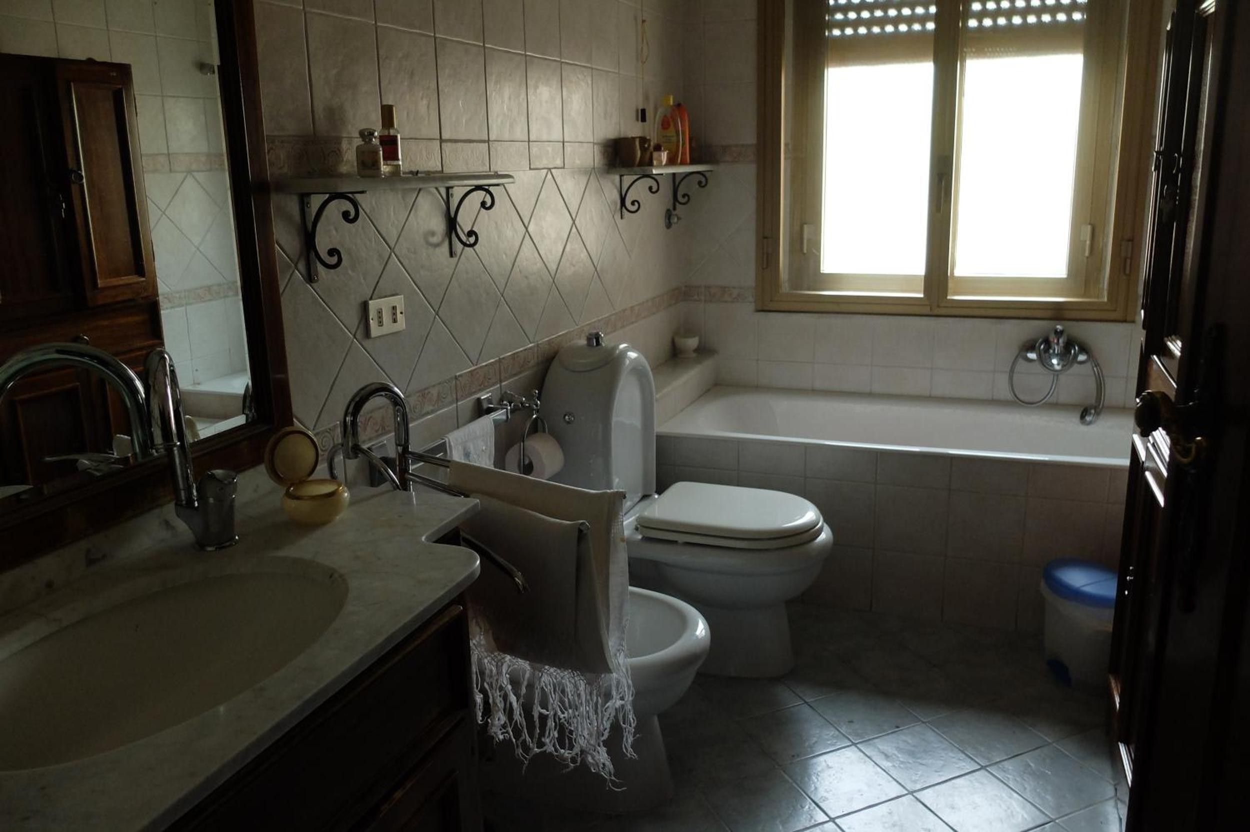 Un bagno con WC, lavandino e vasca. Sopra il WC ci sono mensole con articoli da toilette.