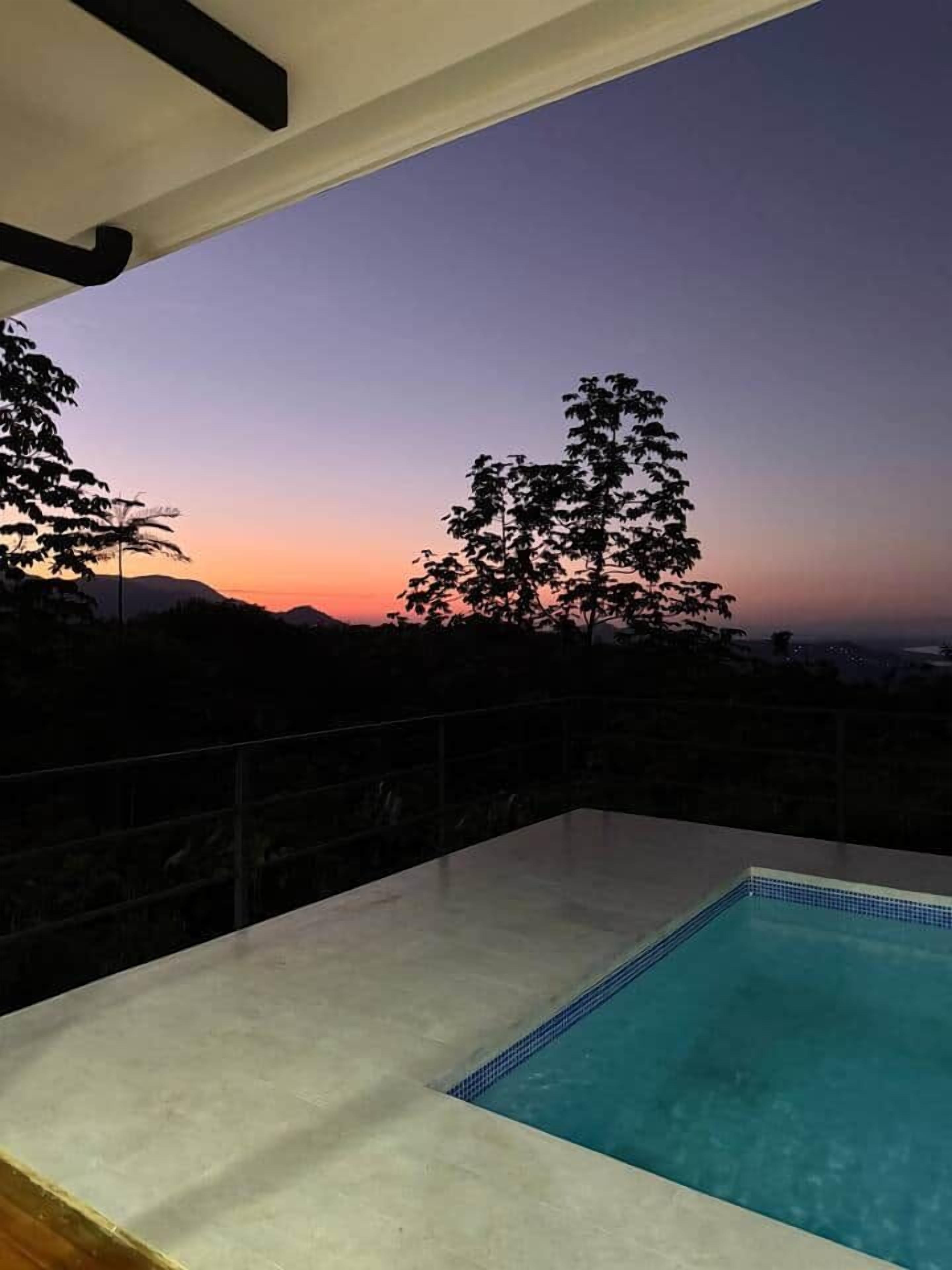A swimming pool with a view of a sunset and mountains in the background.