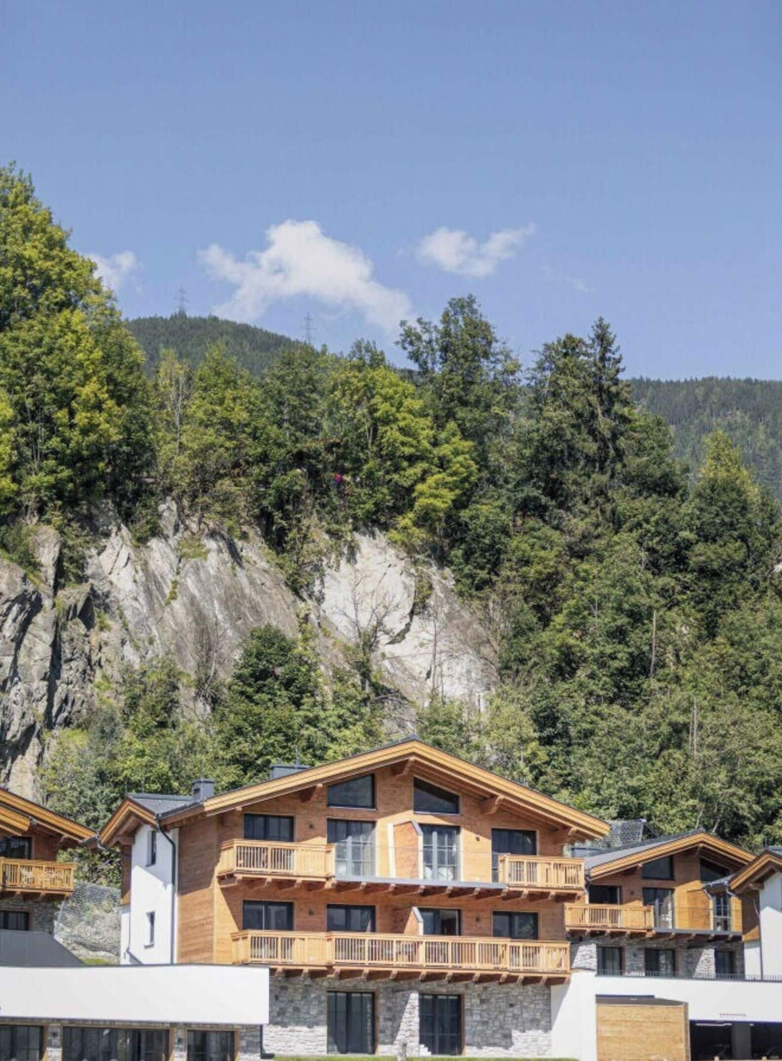 A multi-story building with balconies, set against a backdrop of a forested mountain.
