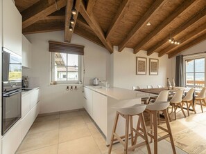 Cozinha moderna com ilha central, vigas de madeira e área de jantar com cadeiras.