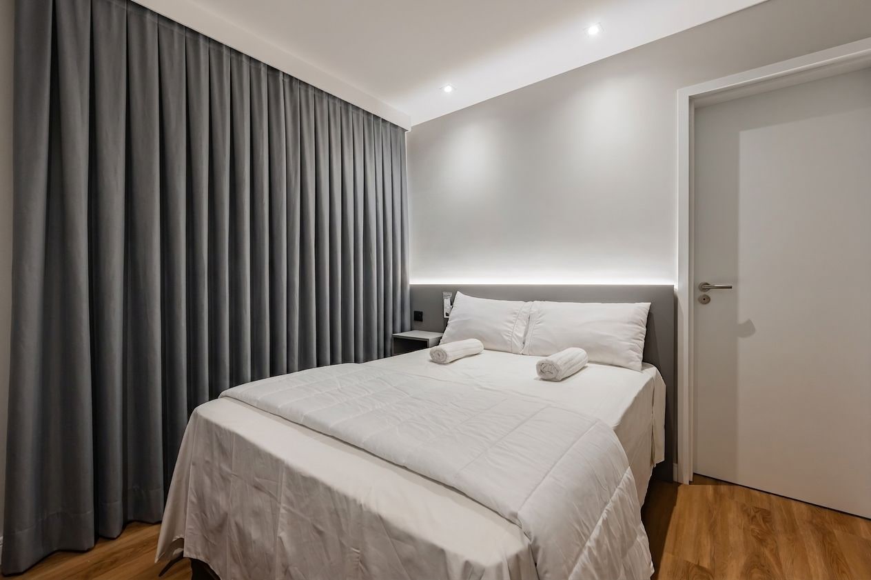 A hotel room with a bed, a nightstand, a door, and a window with curtains.