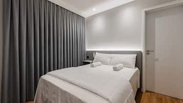 A hotel room with a bed, a nightstand, a door, and a window with curtains.