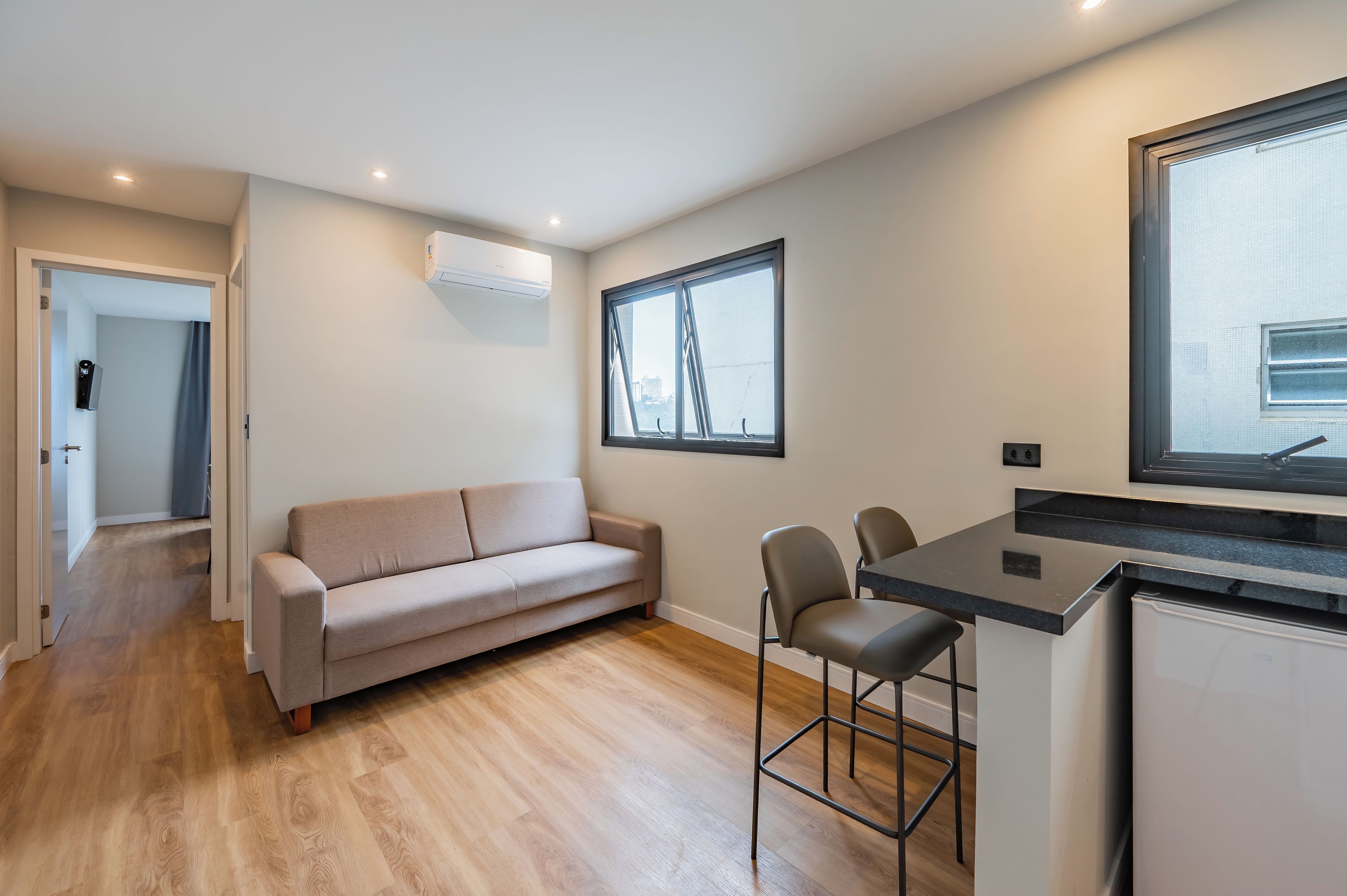 Een moderne leefruimte met een bank, een eethoek met stoelen, een keukenblad en een raam met uitzicht.