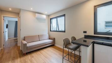 Een moderne leefruimte met een bank, een eethoek met stoelen, een keukenblad en een raam met uitzicht.