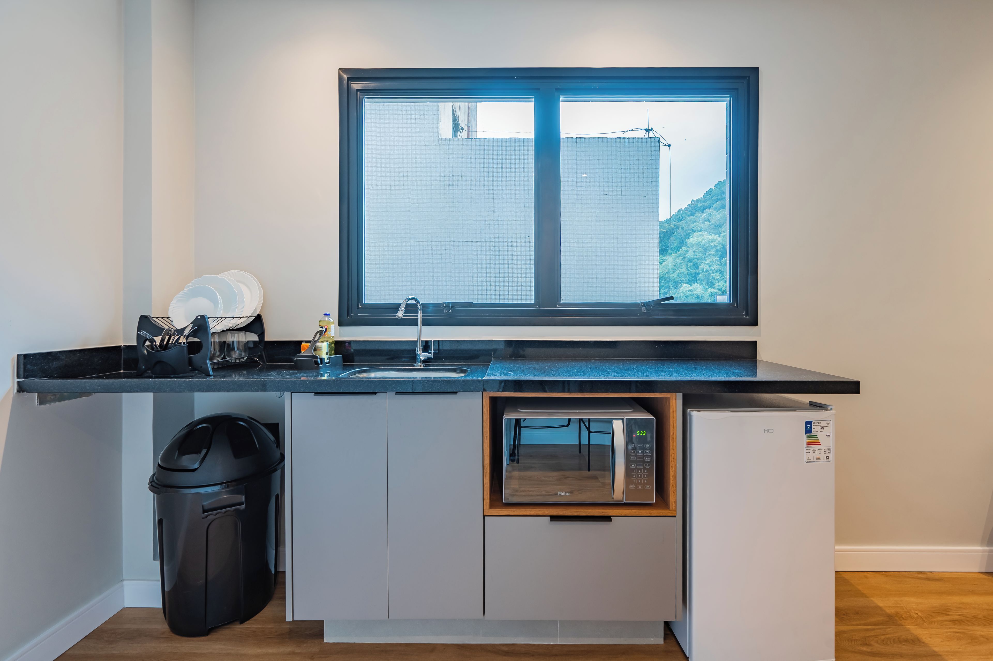 Een compacte keuken met een inbouwmagnetron, een spoelbak en een raam met uitzicht op een stadsbeeld.