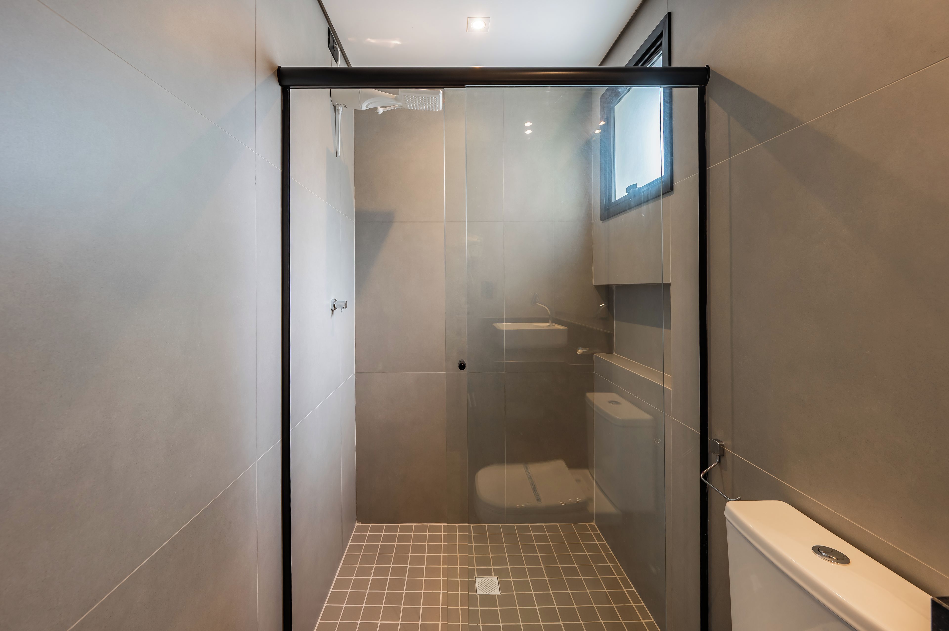 Un baño moderno con ducha separada por mampara de vidrio, inodoro y lavamanos.