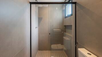 Un baño moderno con ducha separada por mampara de vidrio, inodoro y lavamanos.