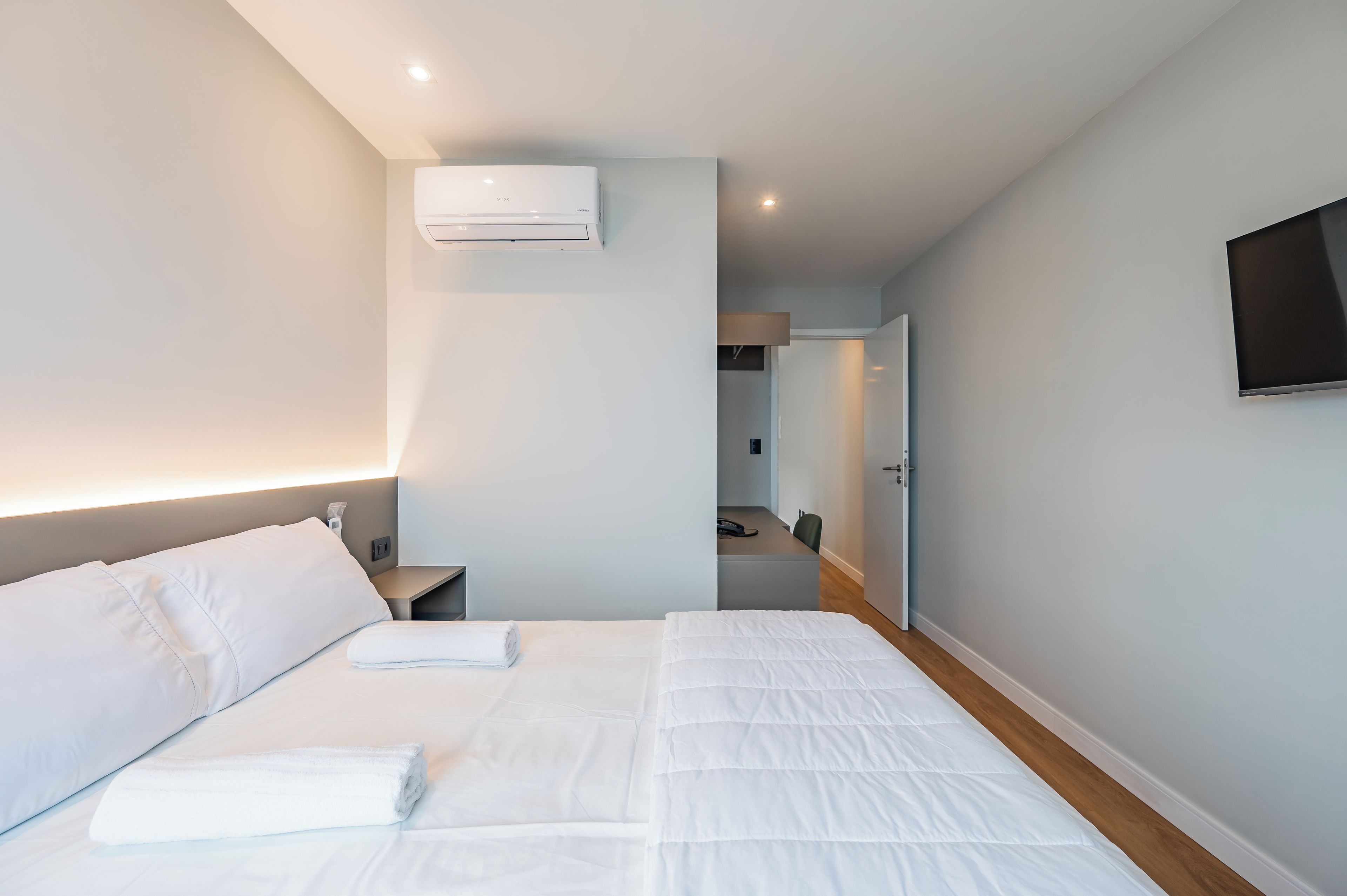 Une chambre d’hôtel moderne équipée d’un lit, d’une table de chevet et d’un téléviseur fixé au mur.