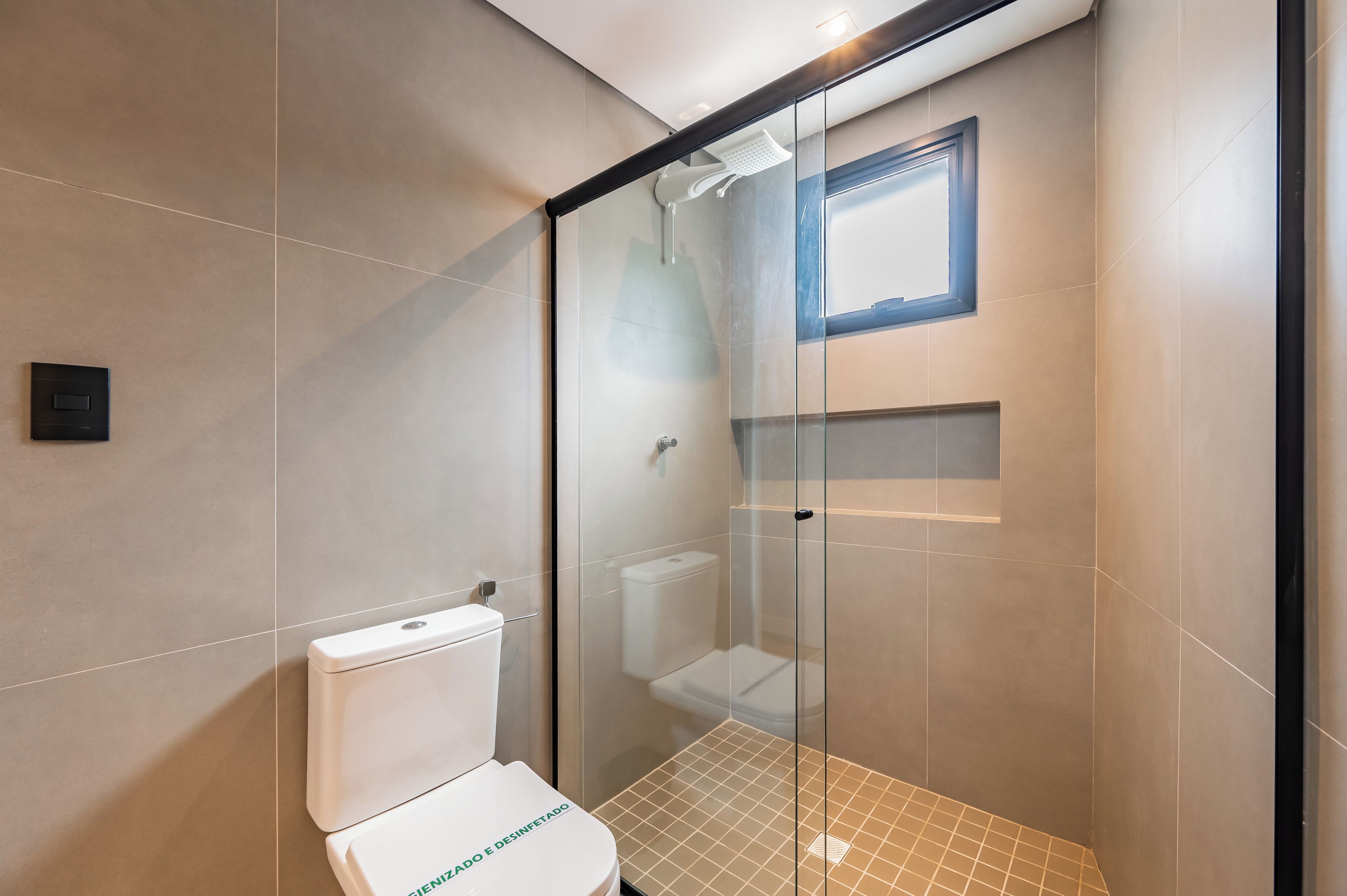 Ein modernes Badezimmer mit einer Duschkabine aus Glas, einer weißen Toilette und einem kleinen Fenster über der Dusche.