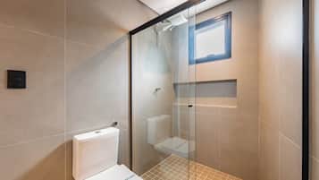 Ein modernes Badezimmer mit einer Duschkabine aus Glas, einer weißen Toilette und einem kleinen Fenster über der Dusche.