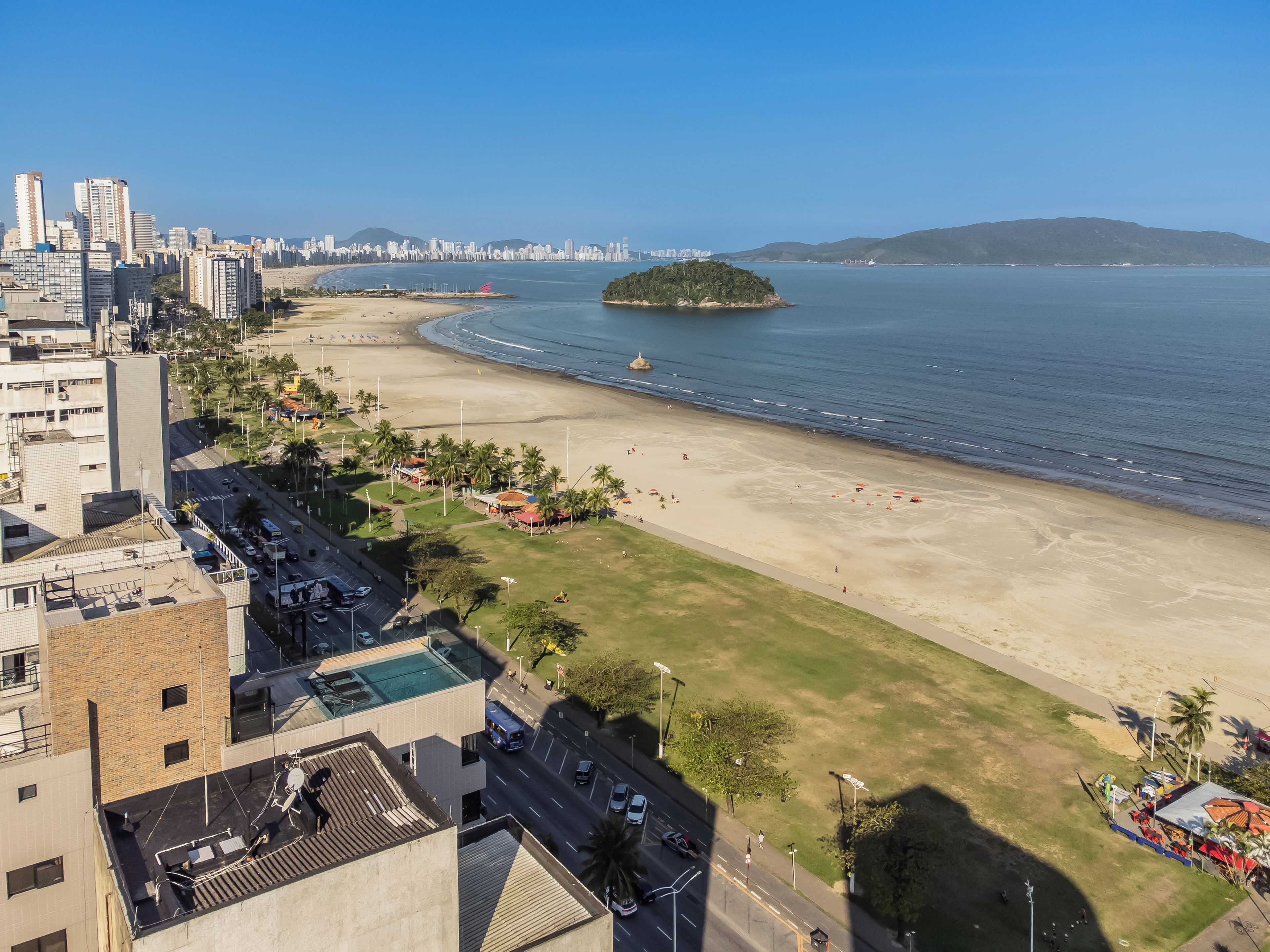 A coastal cityscape with a beach, palm trees, and a distant island.