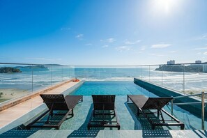 Ein Rooftop-Infinity-Pool mit drei Liegestühlen und ungehindertem Blick auf den Ozean.