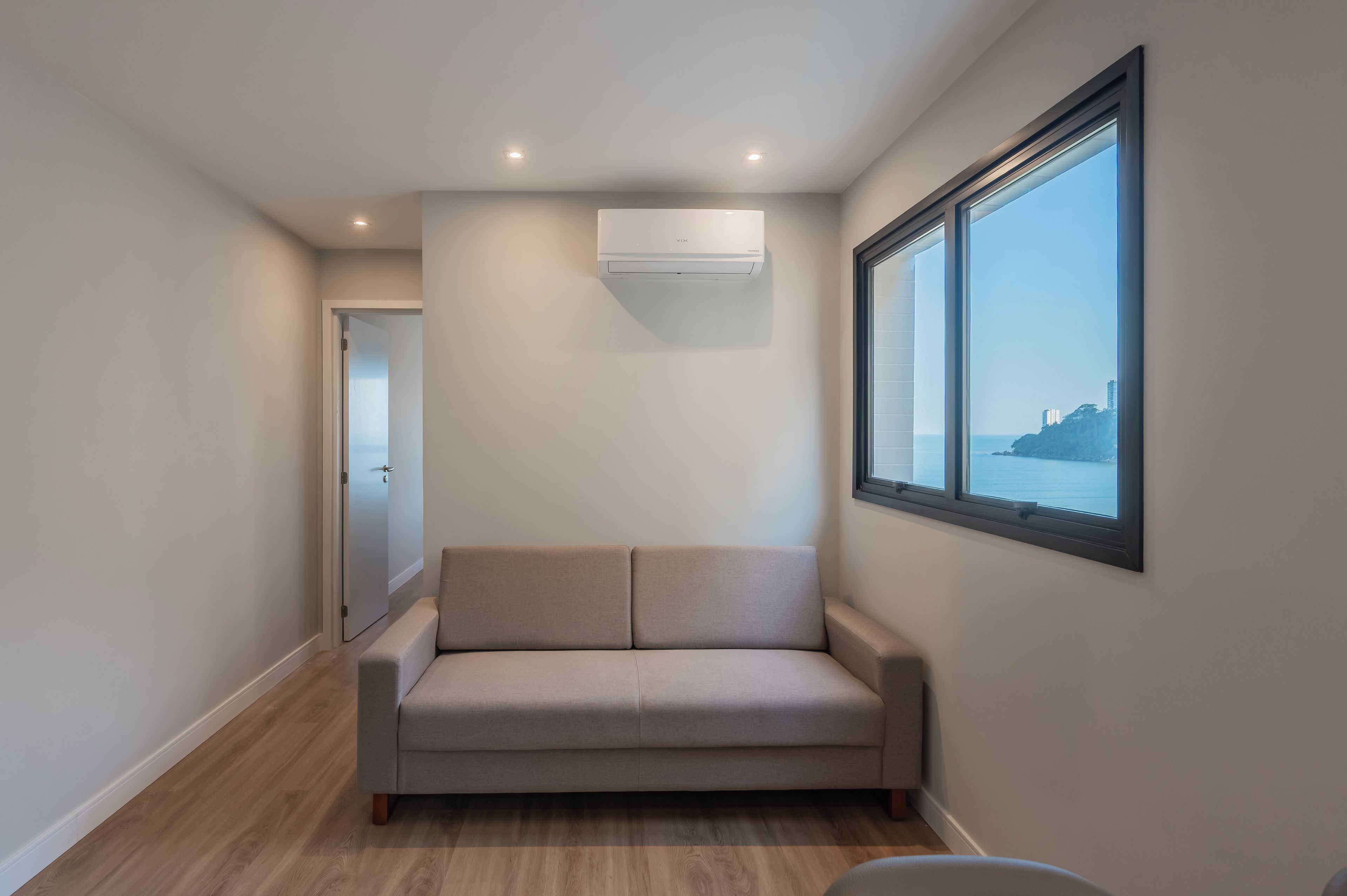 A modern room with a beige sofa, a large window with a view, and an air conditioning unit.