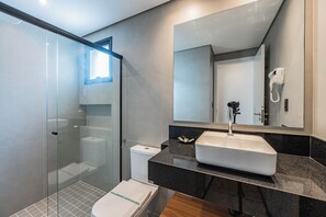 Ein modernes Badezimmer mit einer gläsernen Dusche, einer weißen Toilette und einem Waschbecken mit großem Spiegel darüber.