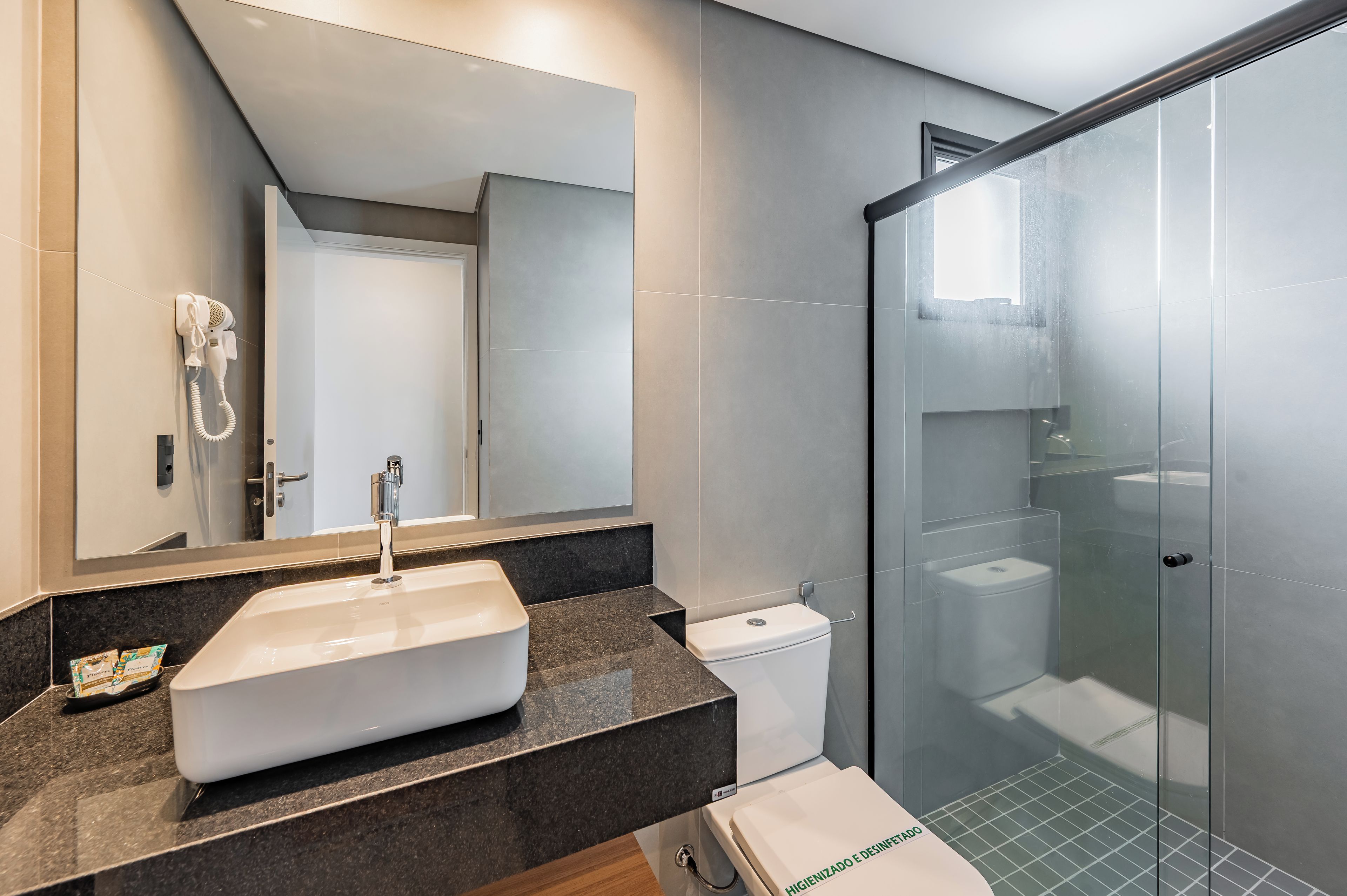 A modern bathroom with a large mirror, a white sink, and a glass-enclosed shower.