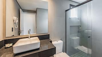 A modern bathroom with a large mirror, a white sink, and a glass-enclosed shower.