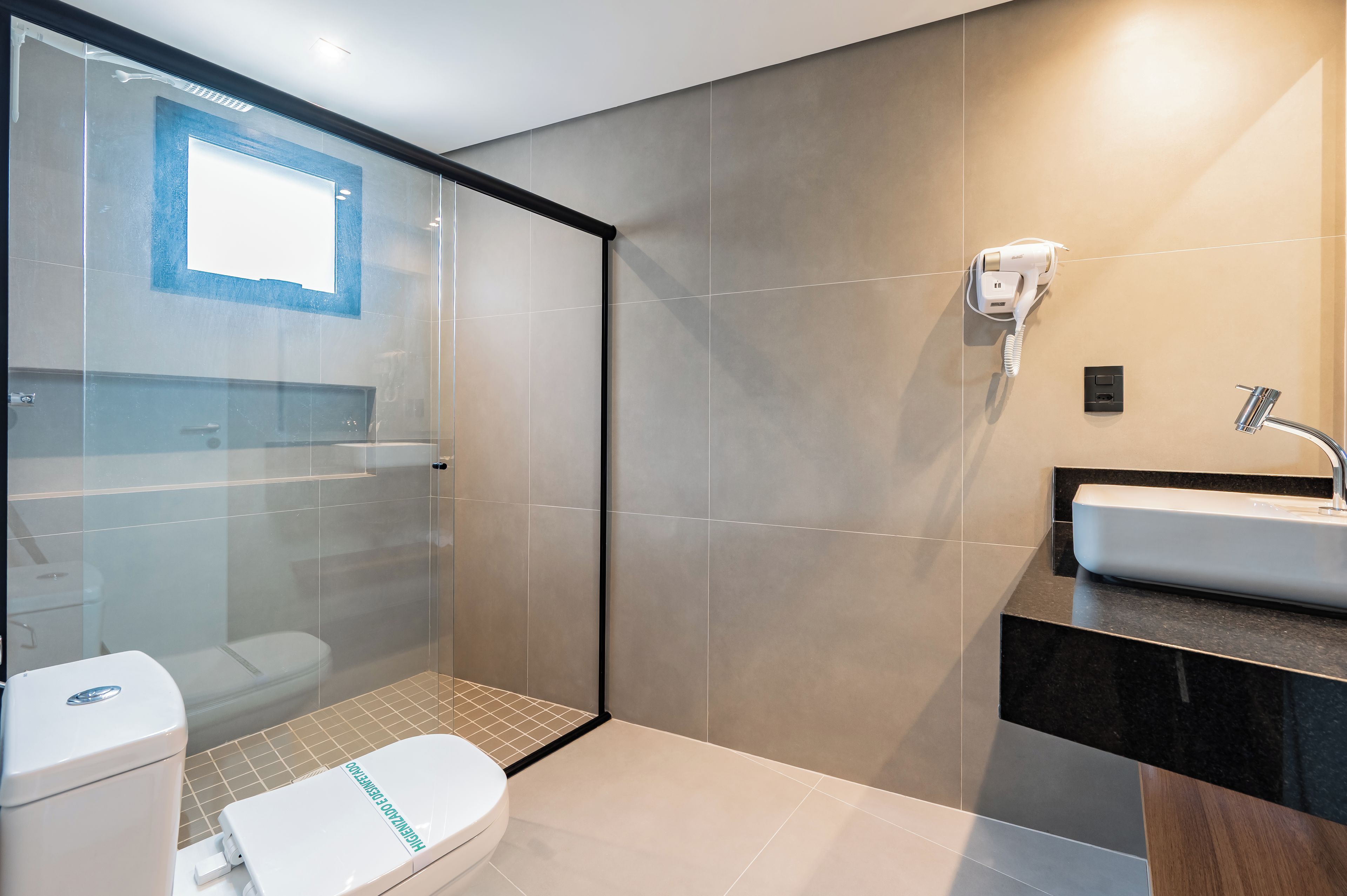 A modern bathroom with a glass shower enclosure, a toilet, a sink, and a hairdryer mounted on the wall.
