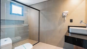 A modern bathroom with a glass shower enclosure, a toilet, a sink, and a hairdryer mounted on the wall.