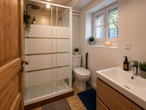Een badkamer met een douchecabine van glas, een toilet, een wastafel met spiegel en een raam met een plant.
