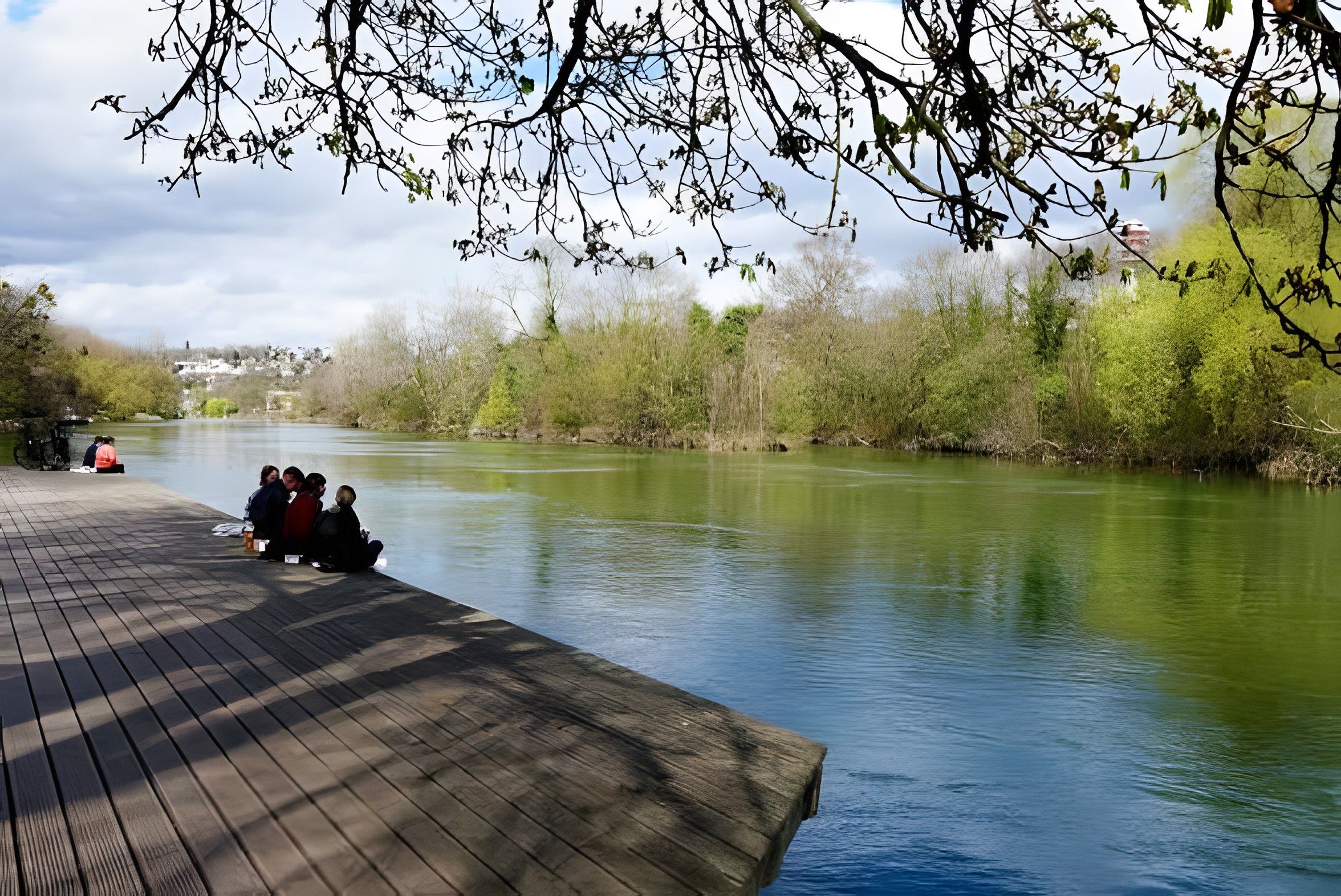 Une rivière paisible avec une jetée en bois où sont assis des gens.