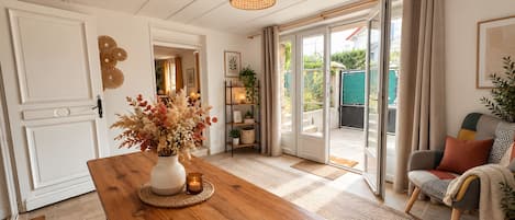 A room with a wooden table, a vase with dried flowers, a hanging light fixture, and a view through a glass door to an outdoor area.