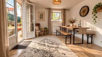 Une pièce comprenant une table à manger, des bancs, un luminaire suspendu, une horloge et une fenêtre avec des rideaux.
