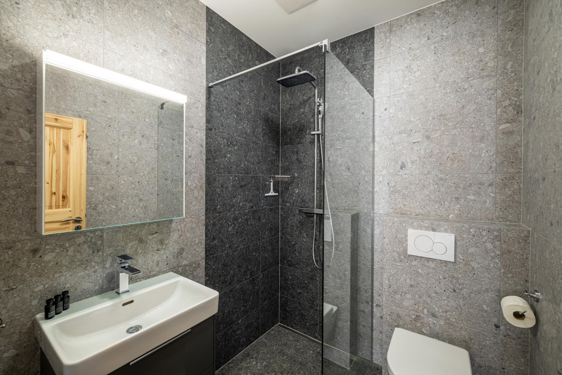 A modern bathroom with a glass-enclosed shower, a white sink, and a wooden door.
