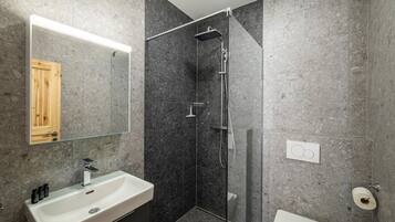 A modern bathroom with a glass-enclosed shower, a white sink, and a wooden door.