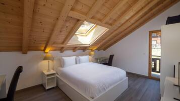 A bedroom with a skylight, a bed, bedside tables, a chair, and a wardrobe.