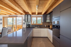 A modern kitchen with a central island, built-in appliances, and a view of the outdoors. - Chalet Bella New Alpine Chalet 8 Guests (Riddes)
