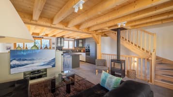 A spacious living area with a wooden ceiling, a fireplace, a sofa, a television, and a kitchen in the background.