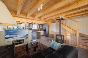 A spacious living area with a wooden ceiling, a fireplace, a sofa, a television, and a kitchen in the background. - Chalet Bella New Alpine Chalet 8 Guests (Riddes)