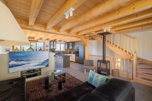 Un amplio salón con techo de madera, chimenea, sofá, televisor y una cocina al fondo.