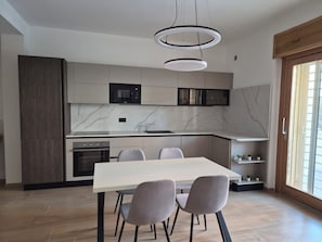 A modern kitchen with a built-in microwave, oven, and a dining area with a table and chairs. - Domus Harmoniae (Albano Laziale)