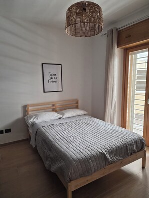 A bedroom with a wooden bed, a woven light fixture, a framed quote on the wall, and a window with curtains.