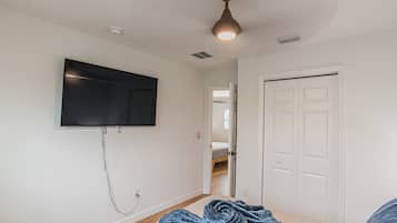 A room with a flat-screen TV mounted on the wall, a ceiling fan, a door, and a bed with a blue blanket.