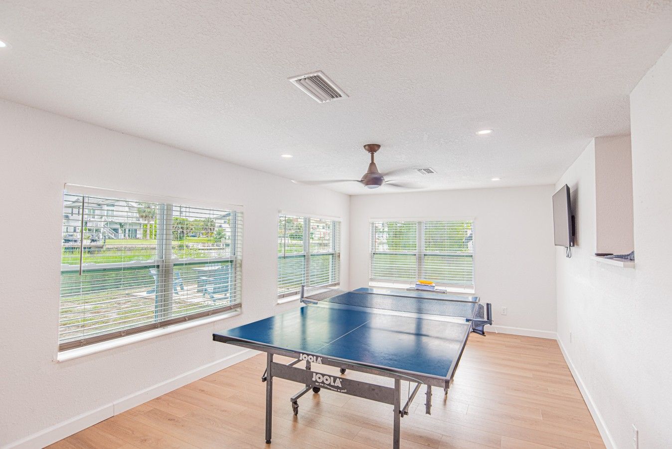 A spacious room with a ping pong table, large windows, and a ceiling fan.