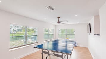 A spacious room with a ping pong table, large windows, and a ceiling fan.