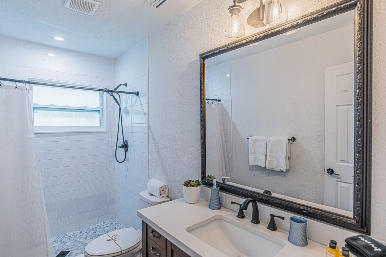 A bathroom with a shower, toilet, sink, and a large mirror.