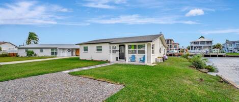 A residential property with a covered patio, a grassy lawn, and a waterfront view.