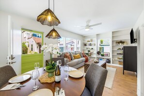 A dining area with a table set for two, a sofa, and a bookshelf. - Labor Day Open - 6 Houses From Sand W/ Parking! (San Diego)