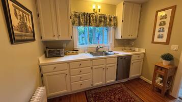 A kitchen with white cabinets, a built-in dishwasher, a window with curtains, and a radiator.