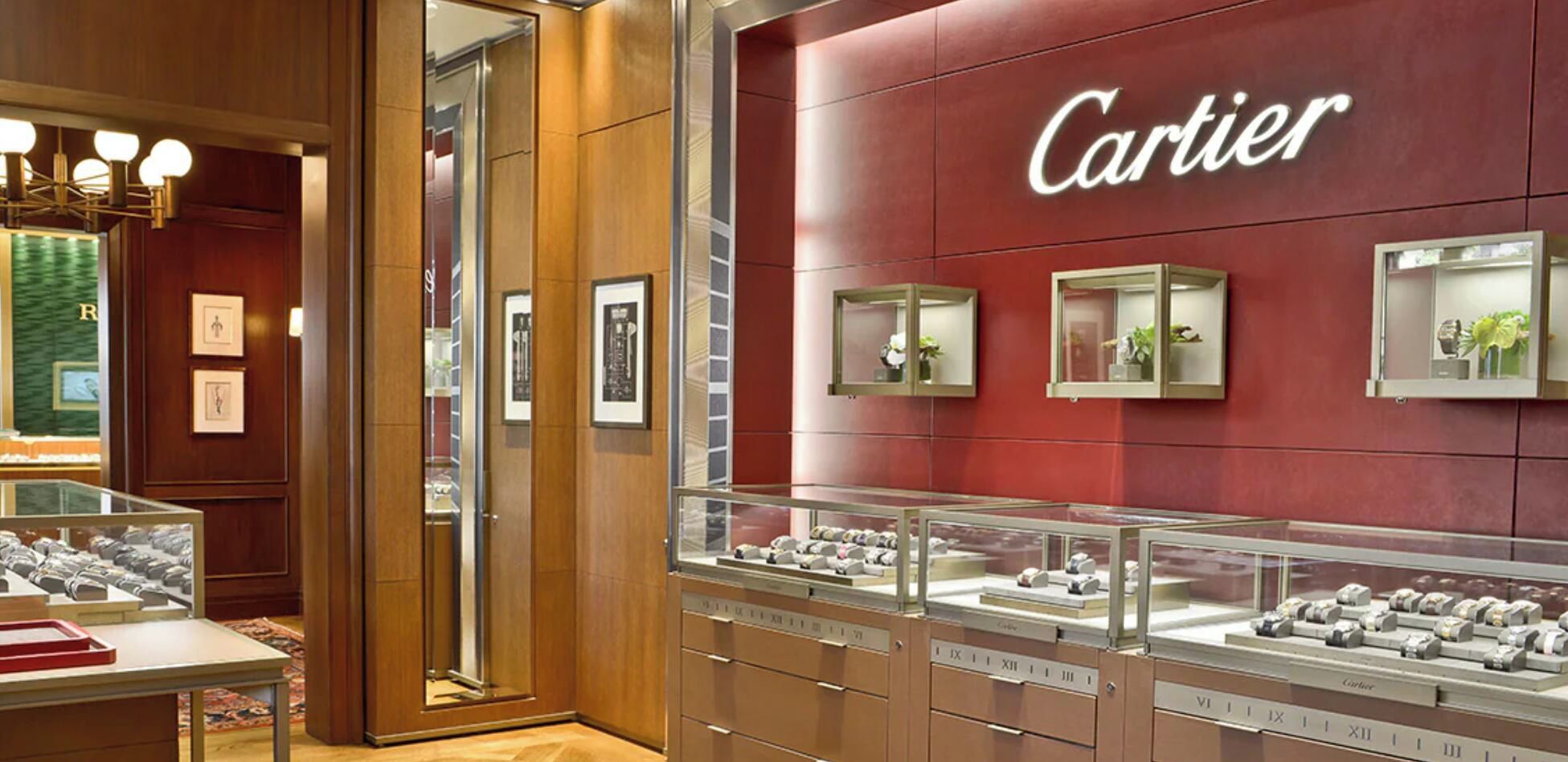 A Cartier store interior with display cases of jewelry, wooden paneling, and a red wall with the Cartier logo.