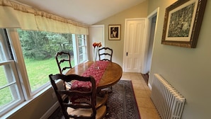 Un coin repas comprenant une table ronde, des chaises, un tapis, un radiateur et une porte donnant sur une autre pièce.
