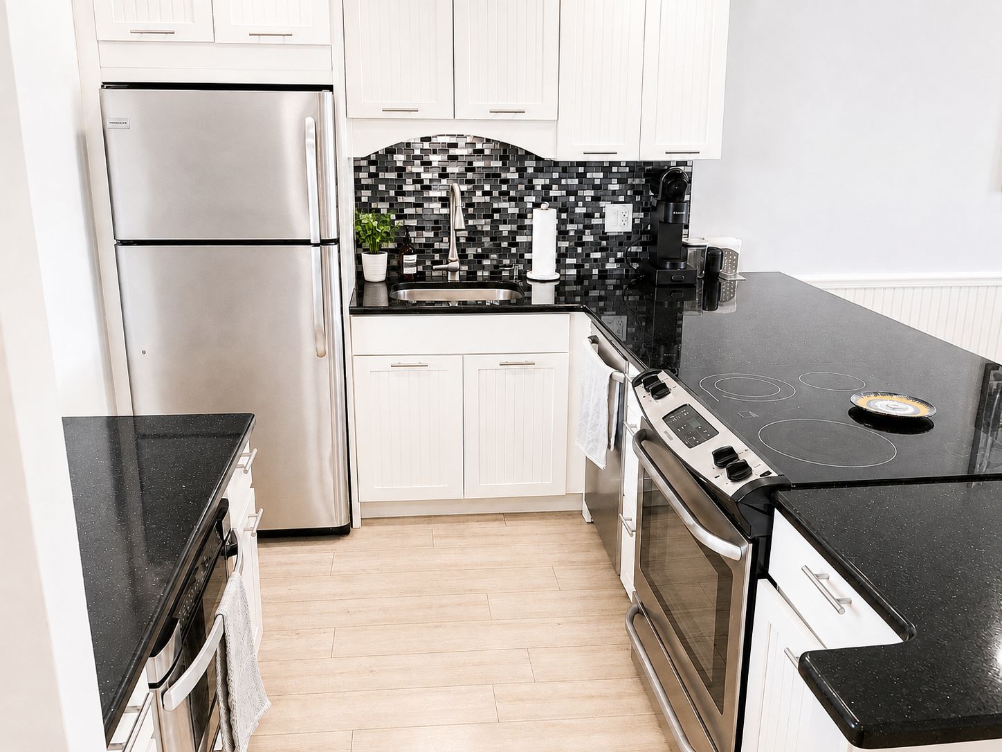 A modern kitchen with stainless steel appliances, a black countertop, and a tiled backsplash.