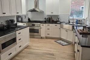 A kitchen with white cabinets, a stainless steel range hood, a built-in oven, a sink, and a window with a view of a brick building. - Luxurious 4-bedroom house in charming neighborhood close to downtown Greensboro. (Greensboro)