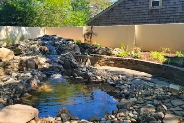 A small pond with a waterfall, surrounded by rocks and plants, with a house in the background. - Luxurious 4-bedroom house in charming neighborhood close to downtown Greensboro. (Greensboro)