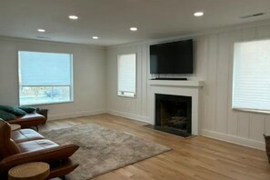 A living room with a fireplace, a television mounted above it, and a large window providing natural light. - Luxurious 4-bedroom house in charming neighborhood close to downtown Greensboro. (Greensboro)